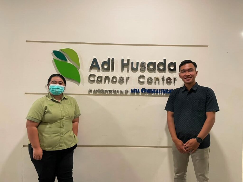 Dokumentasi Mahasiswa Bersama Pembimbing Lapangan di Depan Logo Adi Husada Cancer Center sebagai Lokasi Pelaksanaan Kegiatan Magang