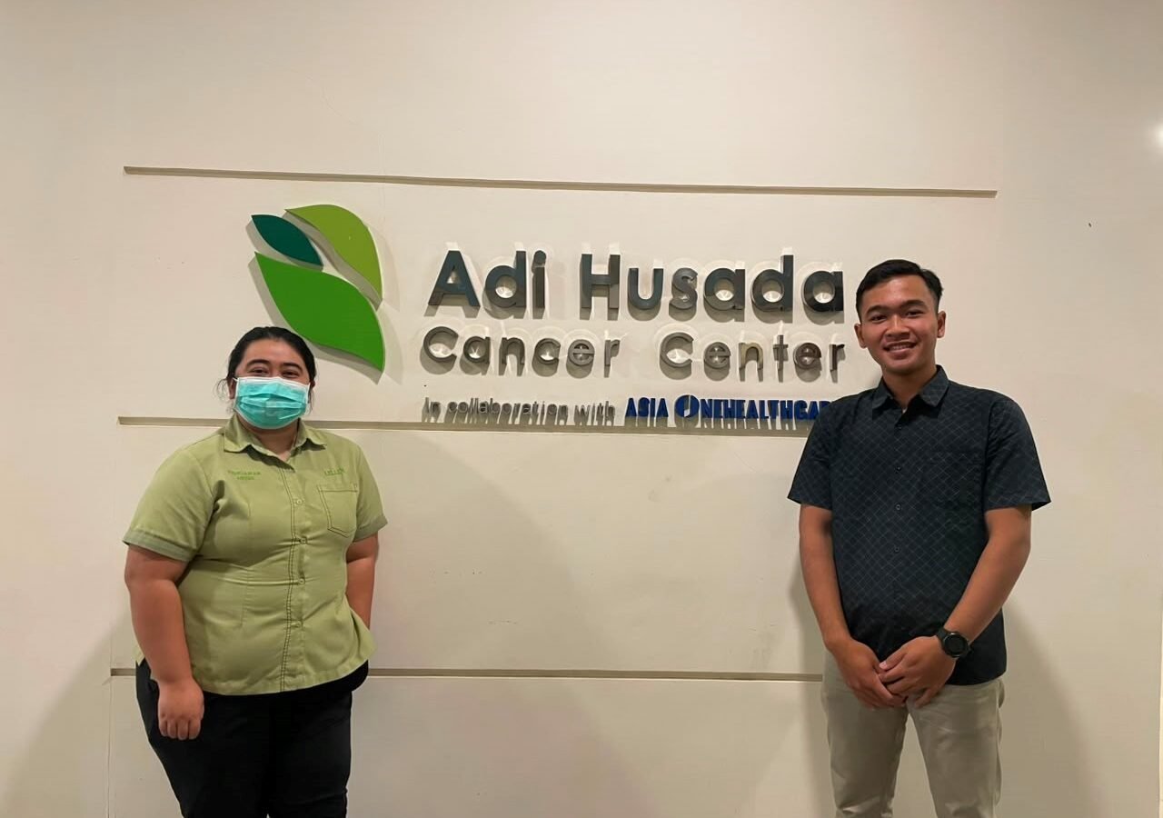 Dokumentasi Mahasiswa Bersama Pembimbing Lapangan di Depan Logo Adi Husada Cancer Center sebagai Lokasi Pelaksanaan Kegiatan Magang