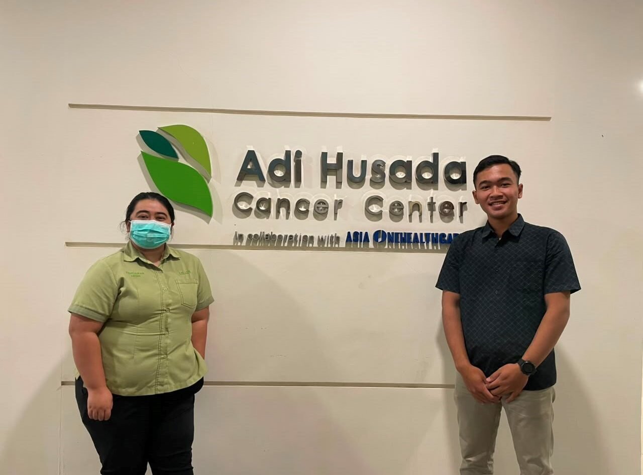 Dokumentasi Mahasiswa Bersama Pembimbing Lapangan di Depan Logo Adi Husada Cancer Center sebagai Lokasi Pelaksanaan Kegiatan Magang