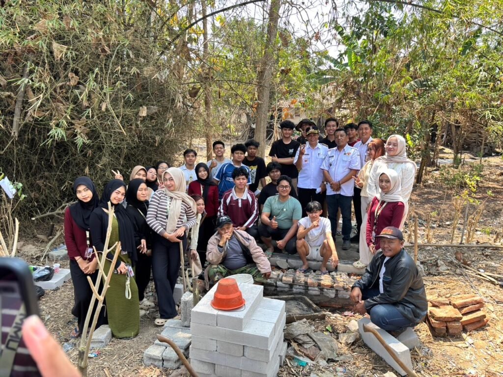 Sebuah foto grup besar yang menampilkan mahasiswa KKN, perangkat desa, dan warga di lokasi pembangunan tungku Rocket Stove di Desa Sumberpetung. Di bagian depan terdapat tumpukan batako sebagai demonstrasi material.