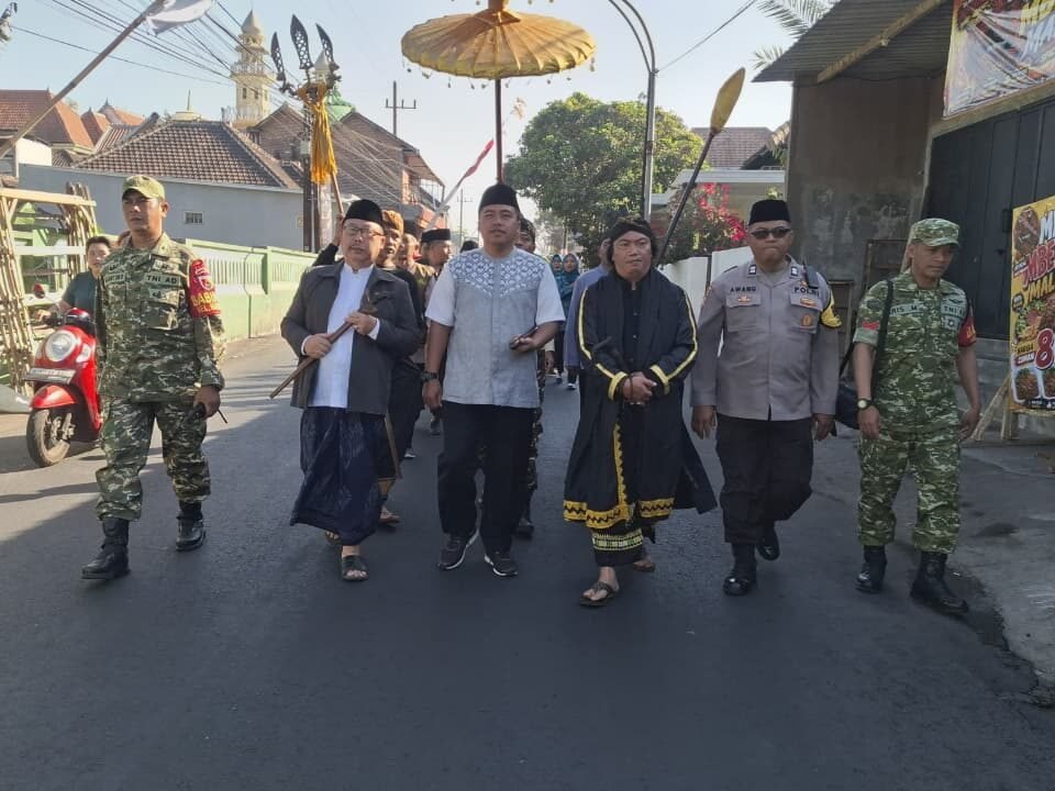 Babinsa Koramil 0833-02/Kedungkandang, Peltu Sugiantoro dan Kopka Aris, bersama aparat kepolisian dan tokoh masyarakat tampak guyub berjalan beriringan mengawal kelancaran prosesi tradisi Bersih Desa.