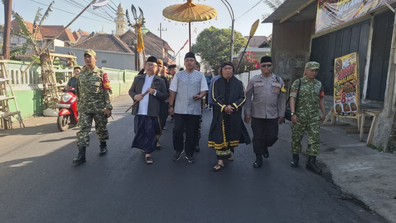 Babinsa Koramil 0833-02/Kedungkandang, Peltu Sugiantoro dan Kopka Aris, bersama aparat kepolisian dan tokoh masyarakat tampak guyub berjalan beriringan mengawal kelancaran prosesi tradisi Bersih Desa.