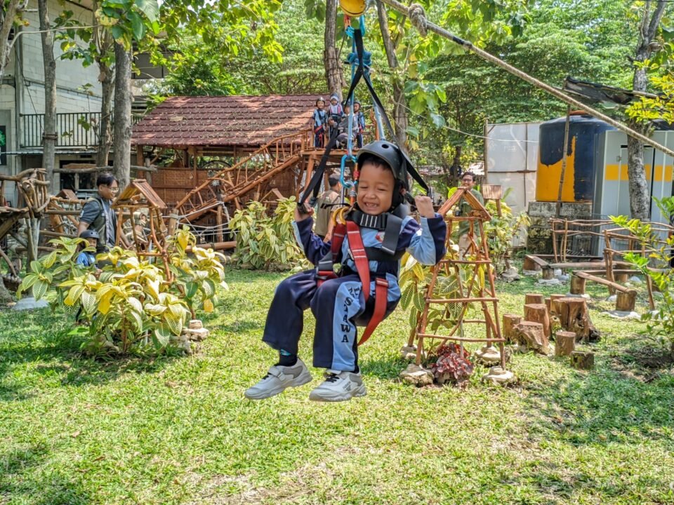 Salah seorang siswa RA Al Mustawa tampak ceria dan berani saat meluncur di wahana flying fox dengan pengamanan lengkap pada kegiatan outing class di Wisata Edukasi Mbedidhink Outbound, Graha BatuBeling, Bojonegoro.