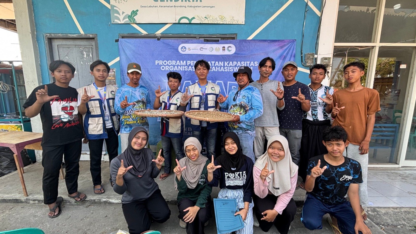 Tim PPK Ormawa BEM Unesa 2026 bersama para petambak, nelayan, dan pemuda Desa Labuhan berfoto bersama sambil memamerkan proses pengeringan ikan rucah dalam rangkaian program Bahari Adiguna, Sabtu (22/8/2026).
