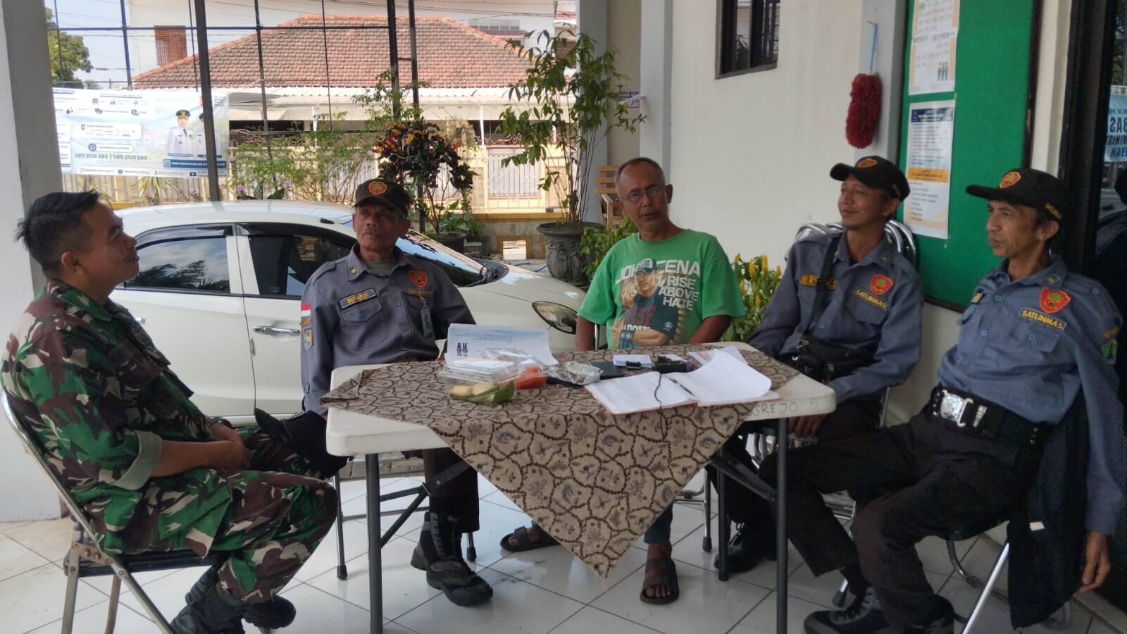 Babinsa Tulusrejo Koramil 0833-05/Lowokwaru, Serda Fajar (kiri), duduk santai sembari berdialog menyerap aspirasi dan berkoordinasi bersama anggota Linmas serta warga di Kelurahan Tulusrejo, Kota Malang, Minggu (20/9/2026).