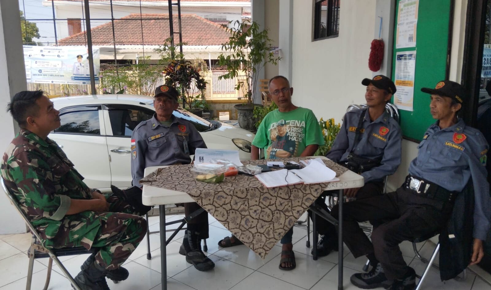 Babinsa Tulusrejo Koramil 0833-05/Lowokwaru, Serda Fajar (kiri), duduk santai sembari berdialog menyerap aspirasi dan berkoordinasi bersama anggota Linmas serta warga di Kelurahan Tulusrejo, Kota Malang, Minggu (20/9/2026).