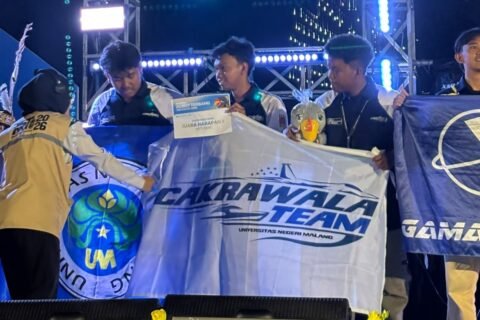 Delegasi Cakrawala Team 2 Universitas Negeri Malang membentangkan bendera kebanggaan usai berhasil meraih Juara Harapan II Divisi Fixed Wing pada ajang bergengsi Kontes Robot Terbang Indonesia (KRTI) 2026.