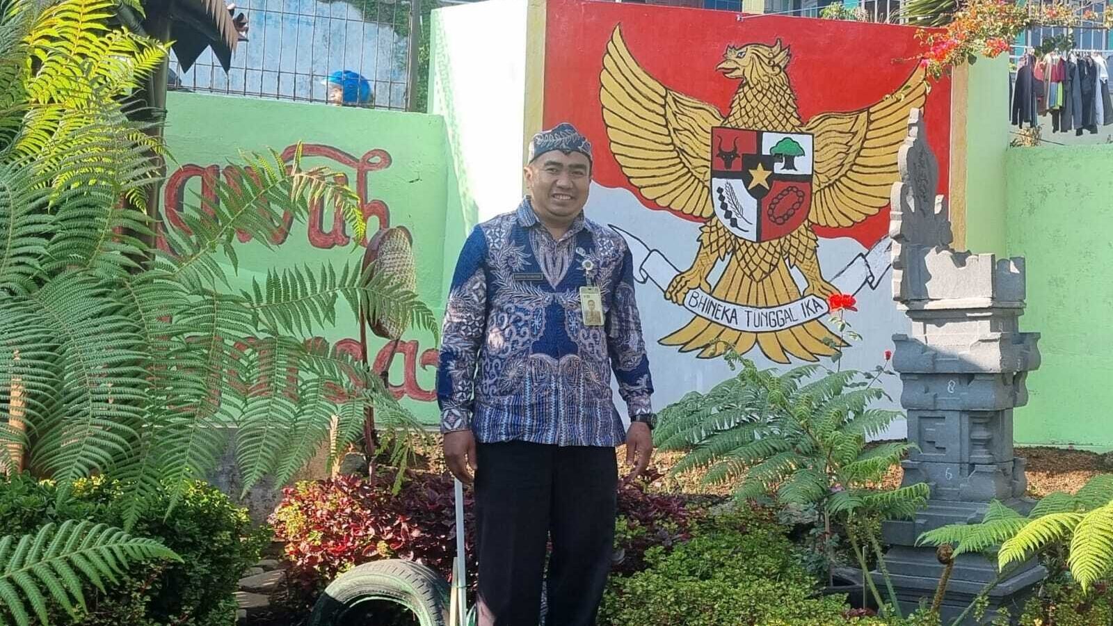 Risdiyan Tri Wahyudi di sudut Kampung Pancasila dengan latar mural Garuda Pancasila dan pelinggih, simbol kerukunan dan keberagaman warga
