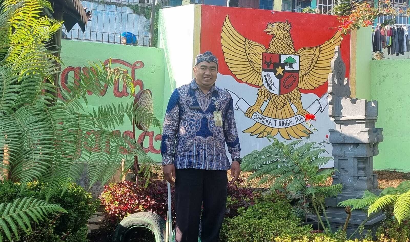 Risdiyan Tri Wahyudi di sudut Kampung Pancasila dengan latar mural Garuda Pancasila dan pelinggih, simbol kerukunan dan keberagaman warga