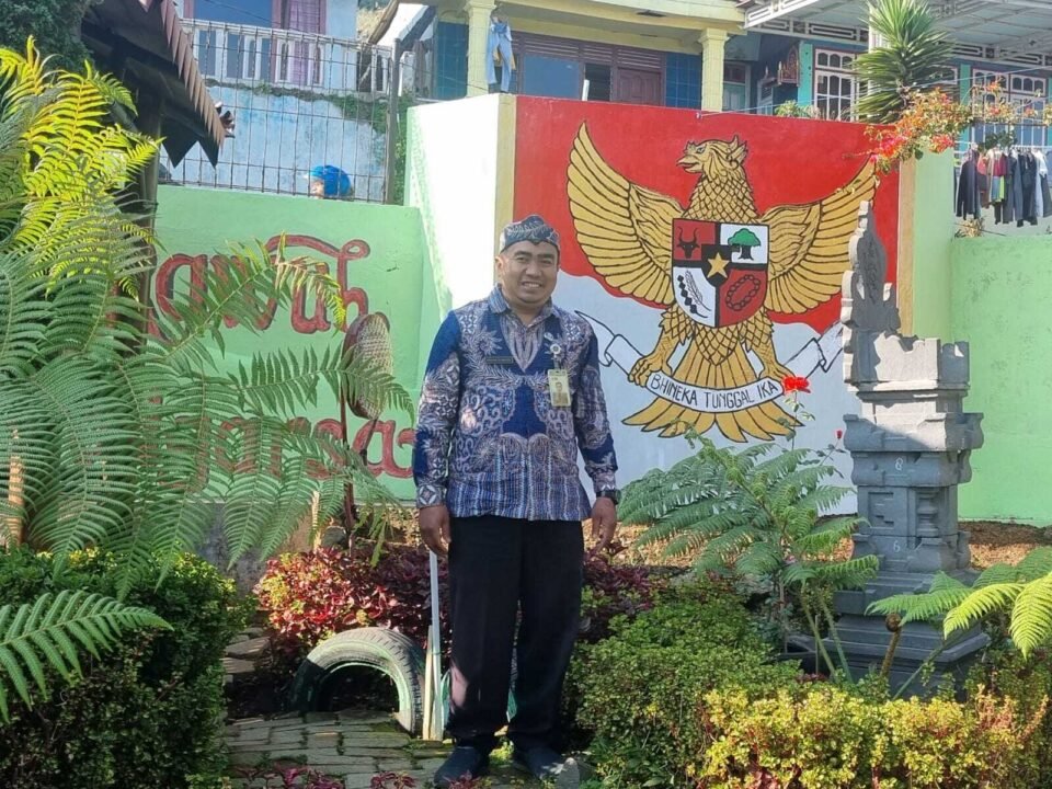 Risdiyan Tri Wahyudi di sudut Kampung Pancasila dengan latar mural Garuda Pancasila dan pelinggih, simbol kerukunan dan keberagaman warga
