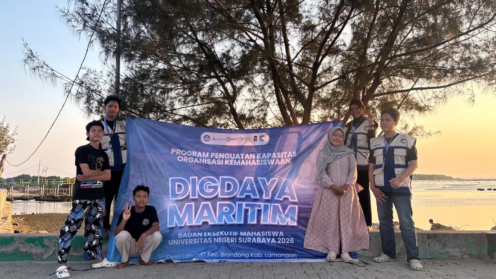 Tim PPK Ormawa BEM UNESA 2026 berfoto bersama perwakilan pemuda Desa Labuhan berlatar senja Pantai Kutang seusai menggelar pelatihan Content Planner & Footage Editing, Minggu (16/8/2026).