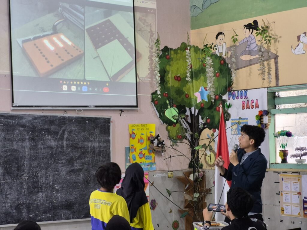 Mahasiswa UB Sosialisasi ke Siswa tentang konsep transformasi luas menggunakan media peraga Lantai Pintar Geometri yang terhubung layar proyektor. (Foto: Dok. Tim PkM UB)