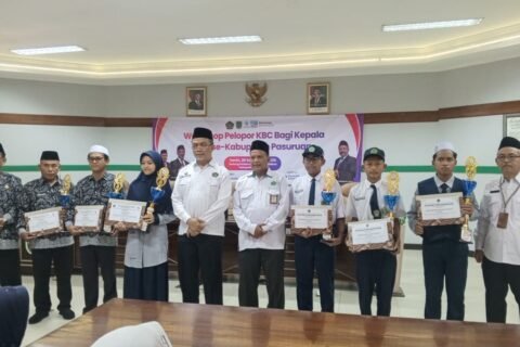 Para siswa berprestasi, termasuk peraih juara OMI 2026 dari MTsN 6 Pasuruan, berfoto bersama Plt. Kepala Kankemenag Pasuruan dan jajaran usai menerima piagam penghargaan serta piala.