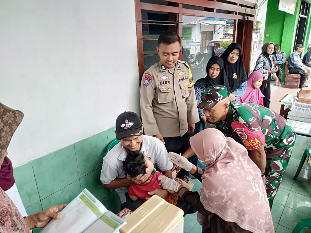 Babinsa Kotalama Koptu Eko bersama Bhabinkamtibmas mendampingi nakes saat memberikan suntikan imunisasi kepada balita dalam layanan Posyandu di Kotalama, Kedungkandang, Kota Malang, Jumat (18/09).