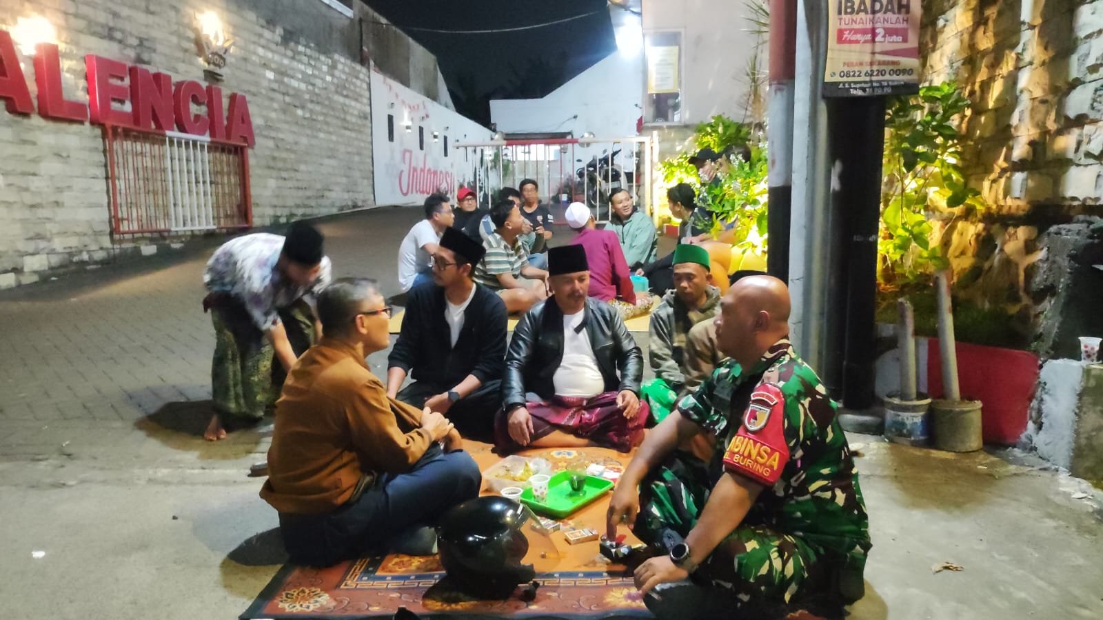 Babinsa Buring, Sertu Arief (kanan depan), tampak membaur dan berbincang gayeng bersama warga di atas gelaran karpet saat melaksanakan giat patroli dialogis malam di wilayah Kelurahan Buring, Kecamatan Kedungkandang, Kota Malang, Rabu malam (16/09/2026).