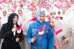 Gubernur Jawa Timur Khofifah Indar Parawansa tersenyum hangat di tengah lautan jamaah Majlis Ta'lim Al-Yasmin Sidoarjo sambil memegang Bendera Merah Putih dalam acara Sholawat Kemerdekaan dan Peringatan Maulid Nabi.