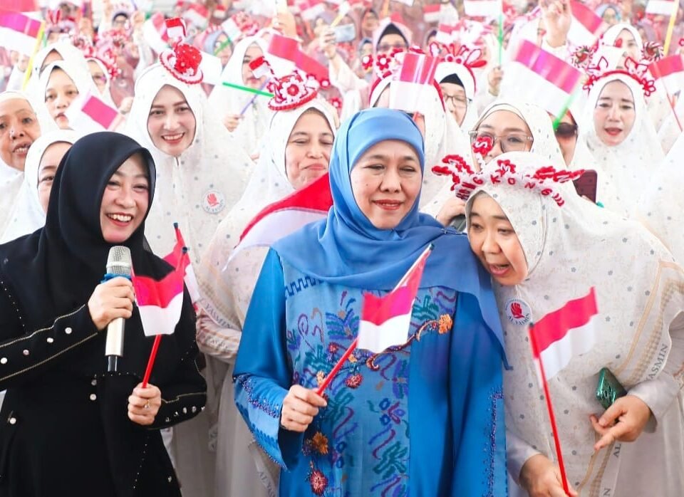 Gubernur Jawa Timur Khofifah Indar Parawansa tersenyum hangat di tengah lautan jamaah Majlis Ta'lim Al-Yasmin Sidoarjo sambil memegang Bendera Merah Putih dalam acara Sholawat Kemerdekaan dan Peringatan Maulid Nabi.