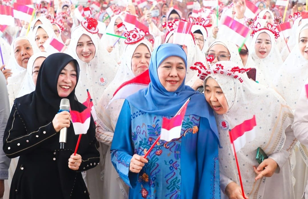 Gubernur Jawa Timur Khofifah Indar Parawansa tersenyum hangat di tengah lautan jamaah Majlis Ta'lim Al-Yasmin Sidoarjo sambil memegang Bendera Merah Putih dalam acara Sholawat Kemerdekaan dan Peringatan Maulid Nabi.