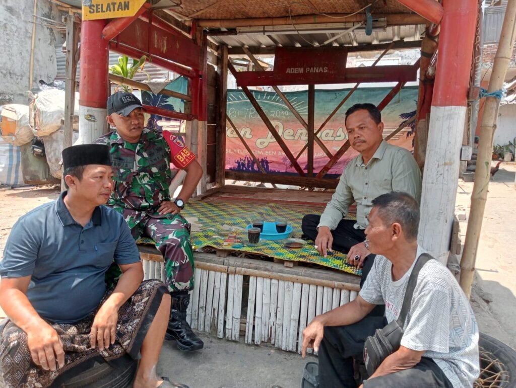 Babinsa Kotalama, Koptu Eko (berjaket loreng), tampak duduk bersama dan berbincang santai penuh kekeluargaan ditemani secangkir kopi bersama sejumlah warga di sebuah pos wilayah Kelurahan Kotalama, Kecamatan Kedungkandang, Kota Malang, Kamis (17/09/2026).