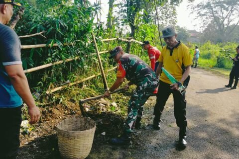 Babinsa Koramil 0833-02/Kedungkandang Serda Sukarji bersama warga bahu-membahu membersihkan rumput liar dan saluran drainase di tepi jalan kawasan Kedungkandang, Kota Malang, Rabu (23/09/2026).