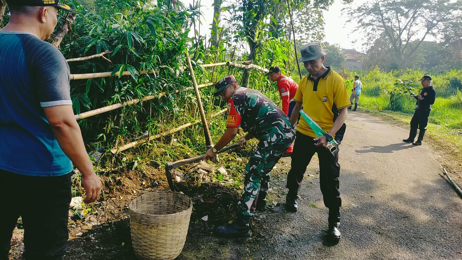Babinsa Koramil 0833-02/Kedungkandang Serda Sukarji bersama warga bahu-membahu membersihkan rumput liar dan saluran drainase di tepi jalan kawasan Kedungkandang, Kota Malang, Rabu (23/09/2026).
