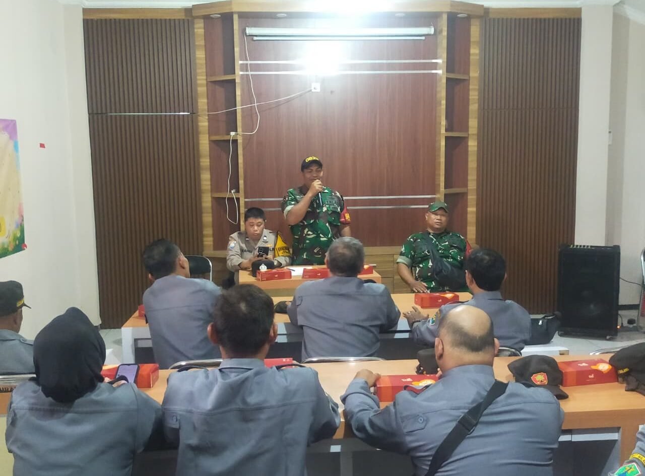 Babinsa Kelurahan Klojen Sertu Gunawan berdiri memberikan arahan dan pembekalan tugas ketertiban wilayah kepada anggota Satlinmas di aula pertemuan, Klojen, Kota Malang.