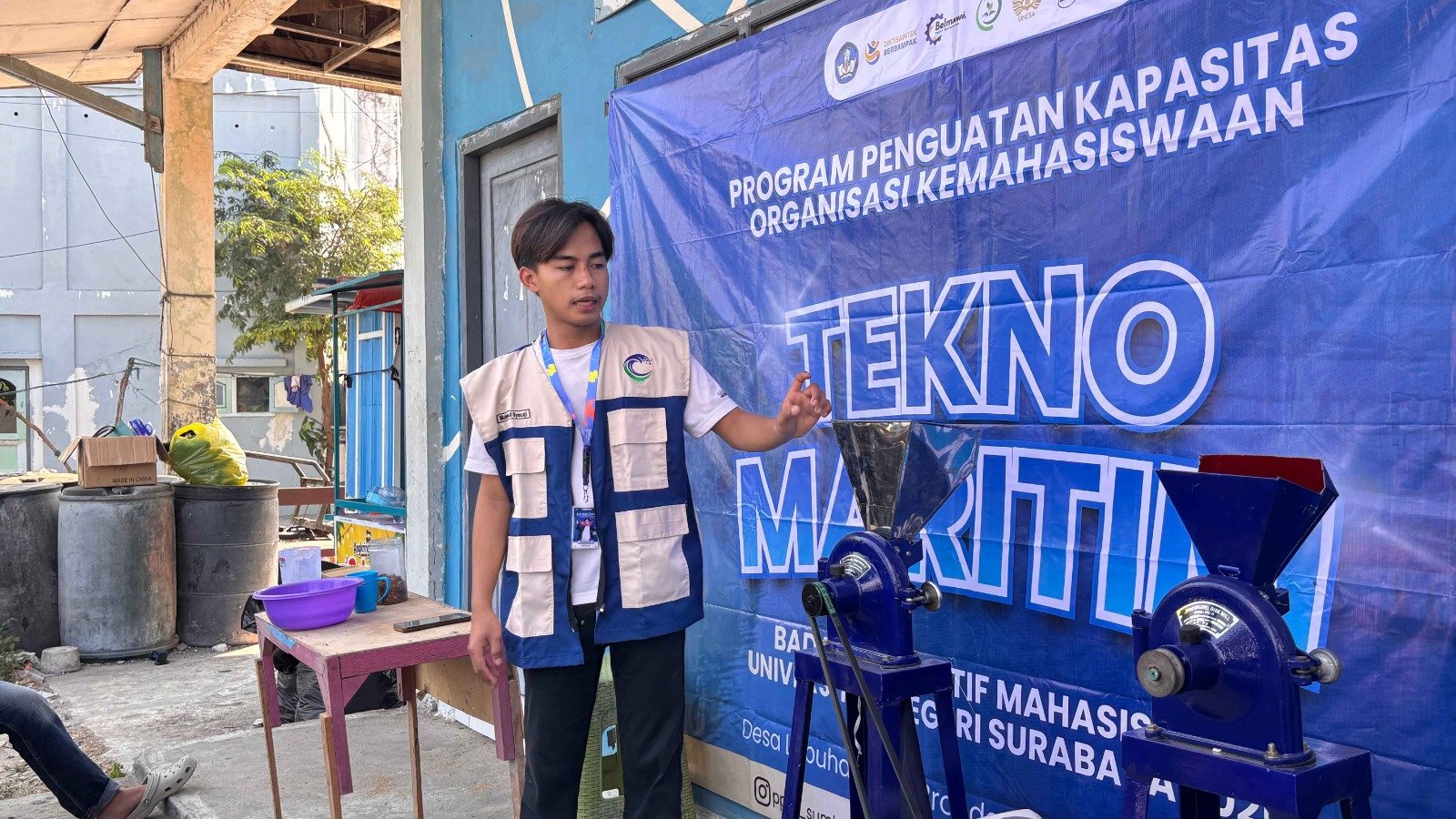 Pemateri dari Tim PPK Ormawa BEM Unesa 2026, Muhammad Syauqi Nasrulloh, mendemonstrasikan operasional Mesin Pengolah 2 in 1 di halaman Rumah Pintar Cendekia Desa Labuhan, Sabtu (22