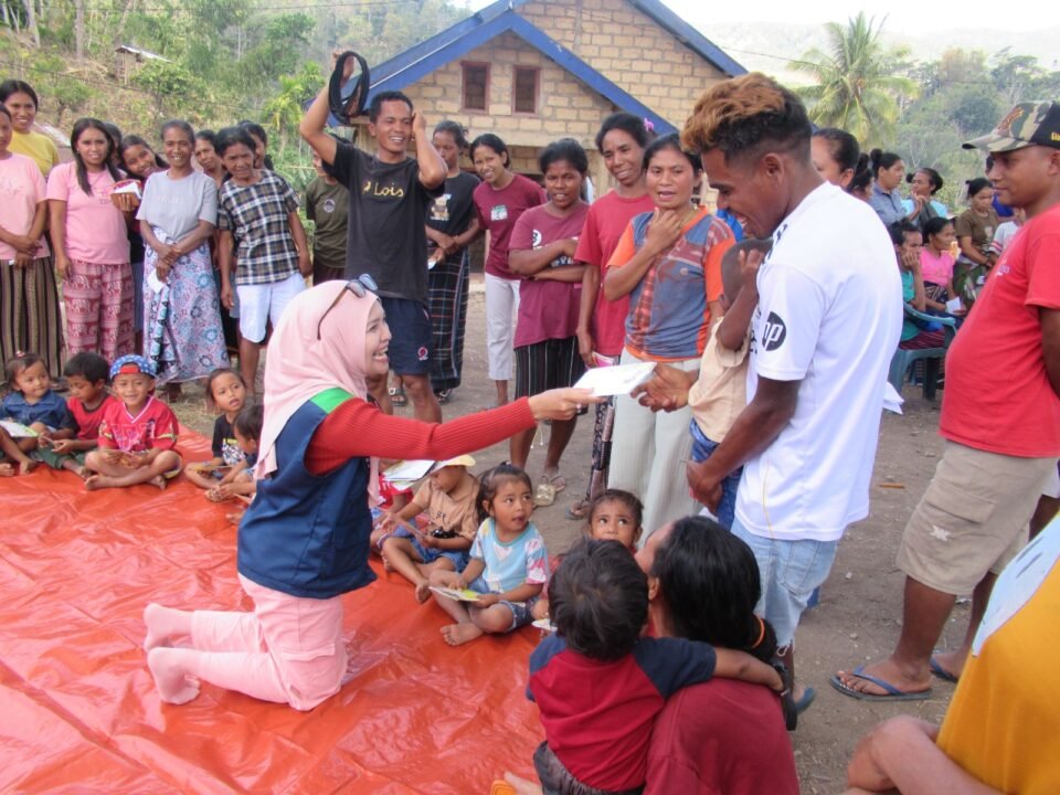 Seorang anggota Tim Relawan Bencana Universitas Negeri Malang (UM) tampak berinteraksi hangat sembari membagikan kertas lipat kepada anak-anak dan warga terdampak gempa dalam sesi Play Therapy di Desa Watunggong, Manggarai Timur.