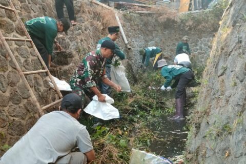 Babinsa Kelurahan Bareng Koramil 0833-01/Klojen, Serka Gatot (berseragam loreng TNI), membaur bahu-membahu bersama puluhan warga membersihkan tumpukan sampah dan sedimen saluran air dalam pelaksanaan GASS di Kelurahan Bareng, Senin (14/09).