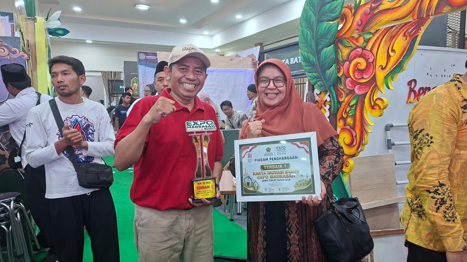 Raut kebahagiaan perwakilan Kemenag Kota Malang saat memamerkan piala dan piagam penghargaan sebagai Terbaik 1 Karya Inovasi Stand Expo Madrasah Jawa Timur 2026 di Surabaya.
