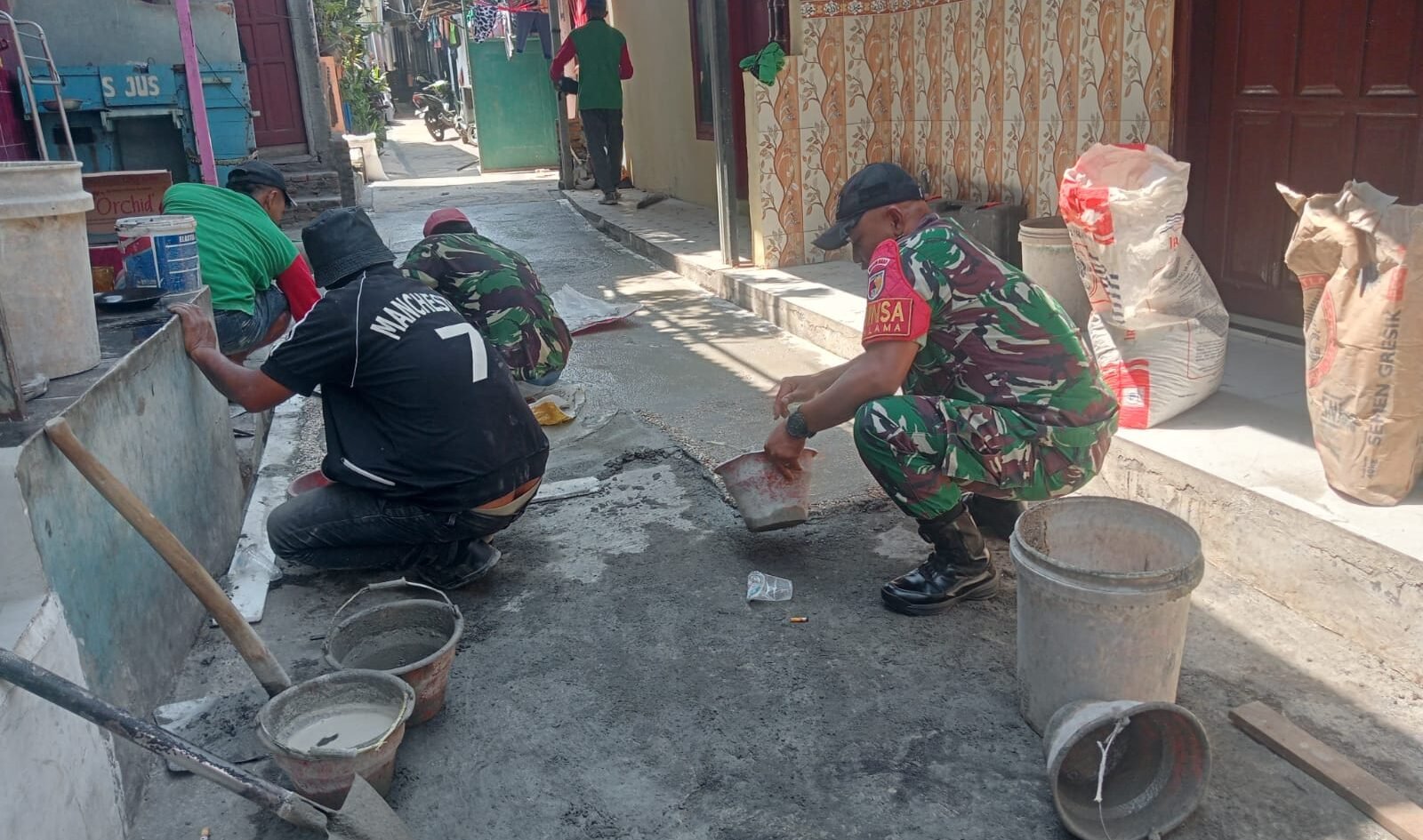Babinsa Kotalama, Koptu Eko, bersama warga setempat, bahu-membahu memperbaiki jalan kampung yang rusak dengan adukan semen di wilayah Kedungkandang, Malang.**