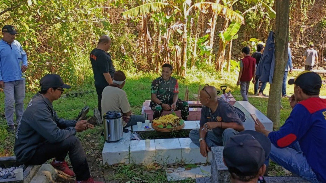 Babinsa Blimbing, Sertu Gede (tengah, seragam loreng), tampak tertawa lepas dan berbincang hangat bersama warga sambil menikmati suguhan sederhana usai kerja bakti membersihkan TPU Kelurahan Blimbing, Kota Malang, Kamis (17/09/2026).