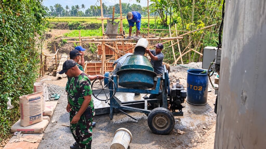 Babinsa bersama warga bahu-membahu mengoperasikan mesin molen dalam pengecoran Jembatan Perintis Garuda.