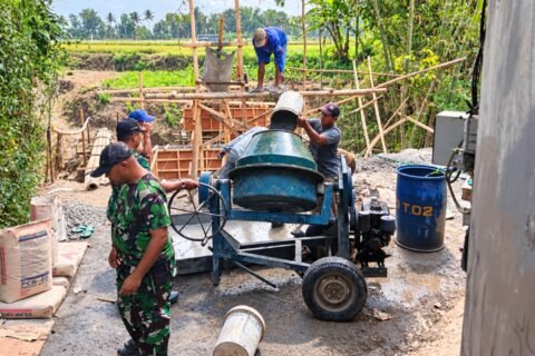 Babinsa bersama warga bahu-membahu mengoperasikan mesin molen dalam pengecoran Jembatan Perintis Garuda.