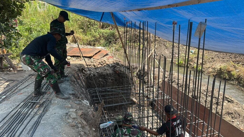 Personel Koramil 0833-05/Lowokwaru bersama warga bergotong royong mempercepat pengecoran pondasi dalam pembangunan Jembatan Perintis Garuda di Kelurahan Tunjungsekar, Kecamatan Lowokwaru, Kota Malang, Jumat (09/10).