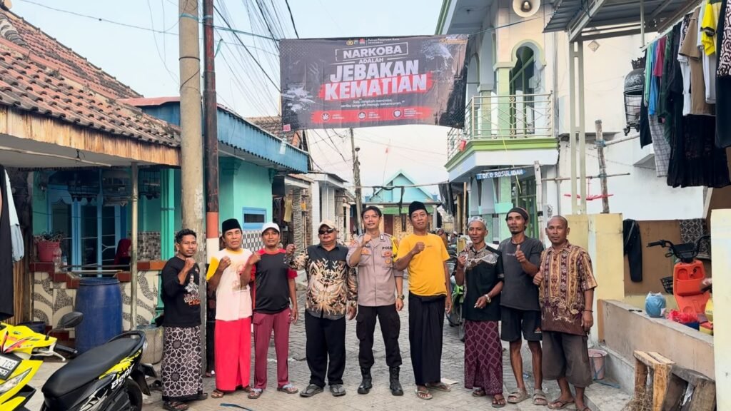 Personel Polres Pasuruan Kota bersama perangkat desa dan warga berfoto bersama di bawah banner imbauan antinarkoba yang telah terpasang.
