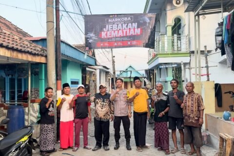 Personel Polres Pasuruan Kota bersama perangkat desa dan warga berfoto bersama di bawah banner imbauan antinarkoba yang telah terpasang.