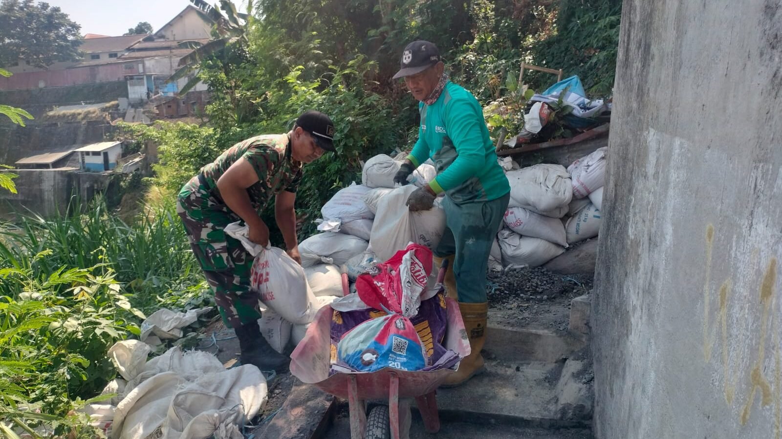 Babinsa Koramil Klojen bersama warga bahu-membahu memindahkan material bangunan di lokasi proyek Jembatan Perintis Garuda.