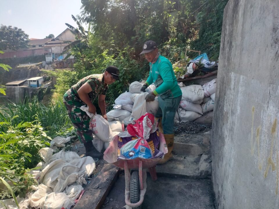 Babinsa Koramil Klojen bersama warga bahu-membahu memindahkan material bangunan di lokasi proyek Jembatan Perintis Garuda.