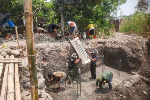 Anggota Koramil 0833-05/Lowokwaru bersama warga bergotong royong menuangkan adukan cor beton secara bertahap pada proses pengecoran pondasi Jembatan Perintis Garuda di Kelurahan Tunjungsekar.