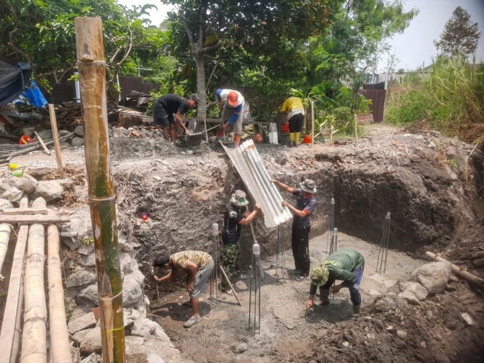 Anggota Koramil 0833-05/Lowokwaru bersama warga bergotong royong menuangkan adukan cor beton secara bertahap pada proses pengecoran pondasi Jembatan Perintis Garuda di Kelurahan Tunjungsekar.