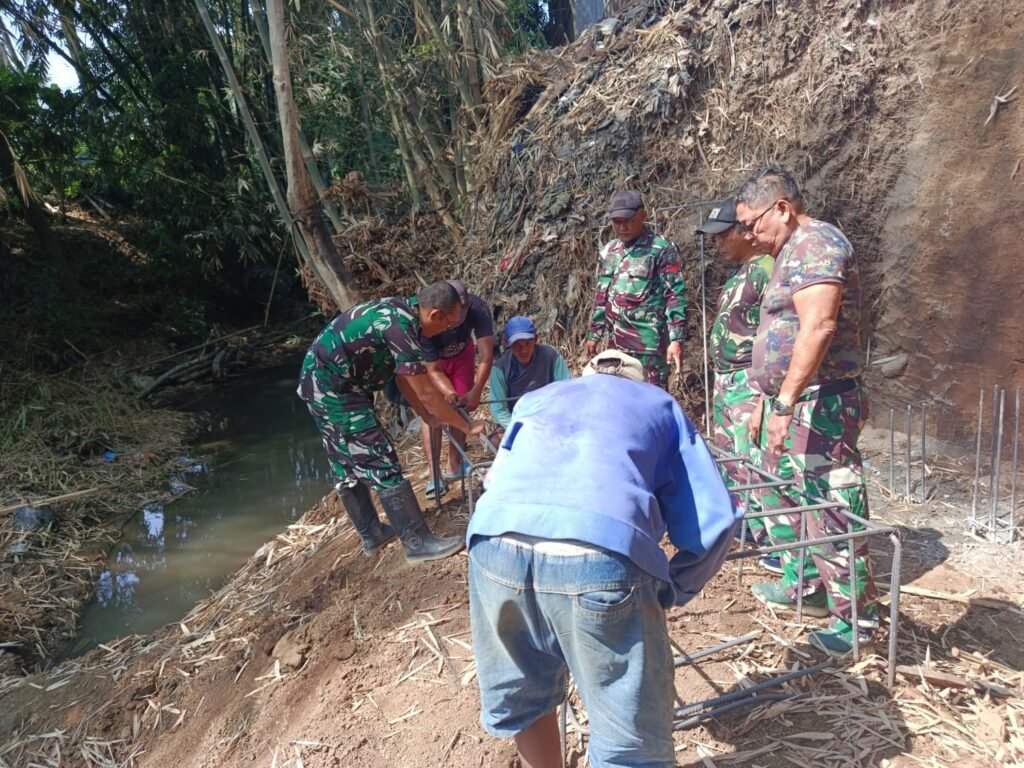 Personel Koramil 0833-02/Kedungkandang bersama warga bahu-membahu merakit kerangka besi pondasi pembangunan Jembatan Perintis Garuda di tepi aliran sungai Kelurahan Cemorokandang, Kecamatan Kedungkandang, Kota Malang, Sabtu (04/10).